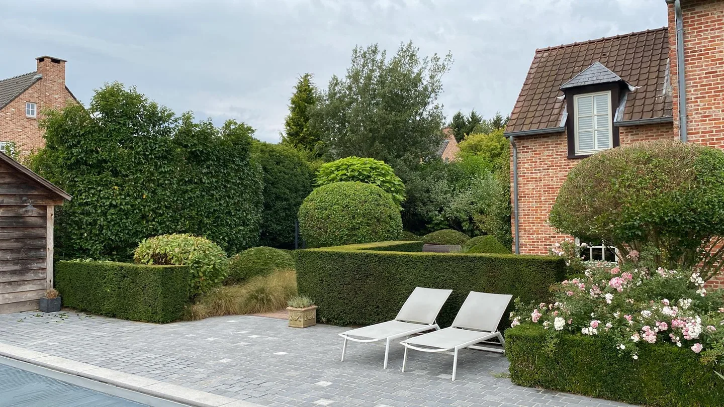 Terrasse en pierre entourée de haies taillées, d’arbustes et de rosiers